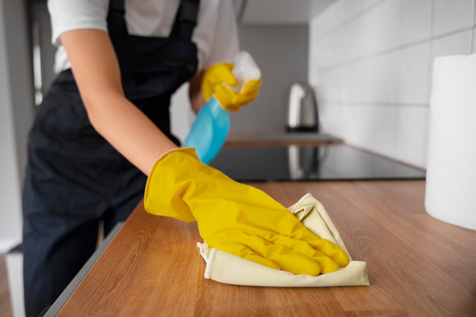 Cleaner wiping kitchen countertop with spray and cloth